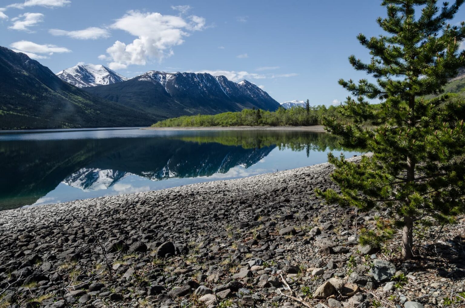 Tranquil lakeside view at Kluane National Park with snow-capped mountains reflecting on the calm water