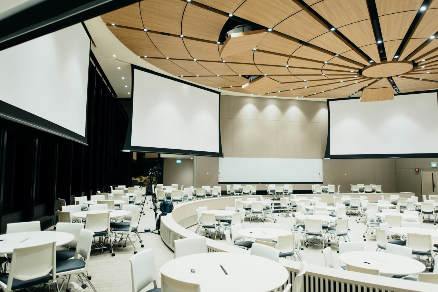 Modern conference hall with large projection screens, advanced audiovisual equipment, and a circular seating arrangement, ready for an event.